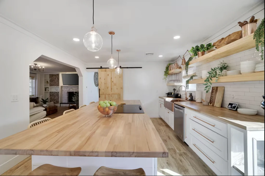 Wide view of the renovated kitchen with butcher-block counters, pendant lights and open shelving